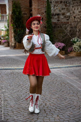 Girl wearing a majorette uniform, outdoors, portrait in hat with red feather and stick. Country of Castellaro Lagusello, Monzambano, Mantua, Italy, Europe. Show annual flower market.