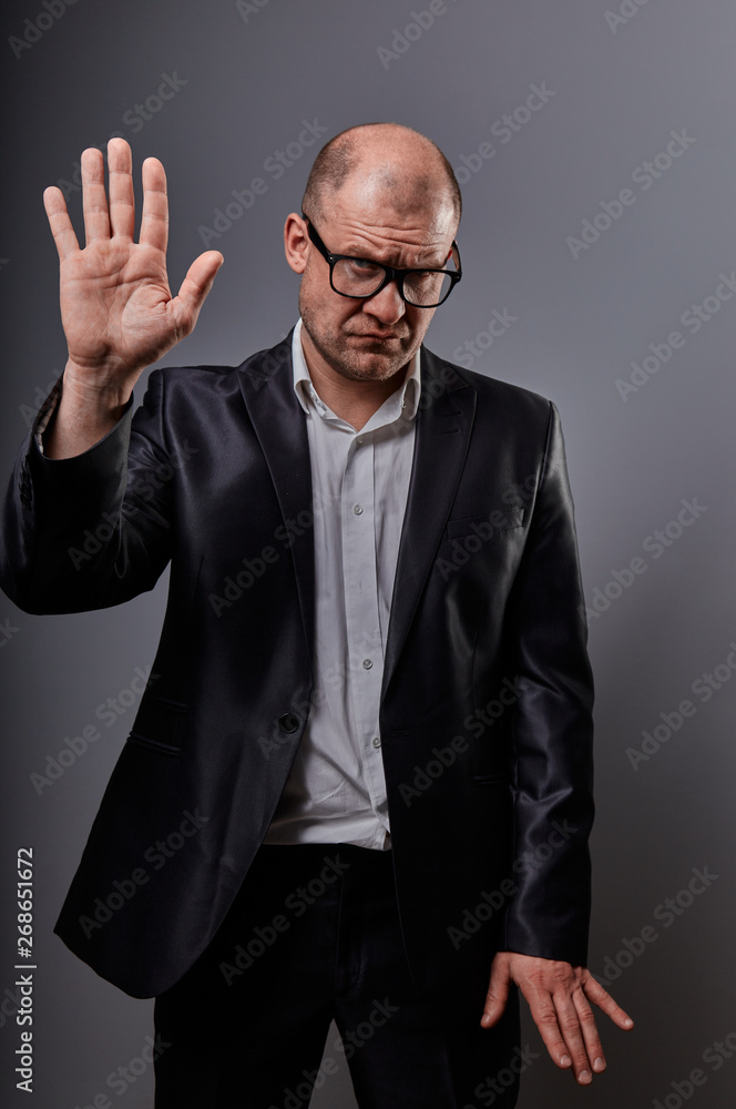 Unhappy depressed busuness man in black suit and glasses showing the palm stop sign on grey background. Closeup Unhappy depressed busuness man in black suit and glasses showing the palm stop sign on grey background. Closeup