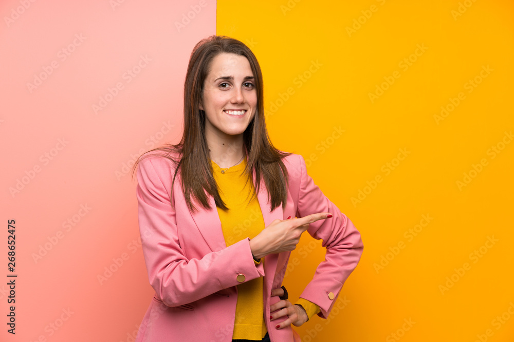 Young woman with pink suit over colorful background pointing finger to the side Young woman with pink suit over colorful background pointing finger to the side