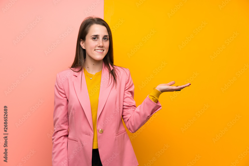 Young woman with pink suit over colorful background holding copyspace imaginary on the palm Young woman with pink suit over colorful background holding copyspace imaginary on the palm