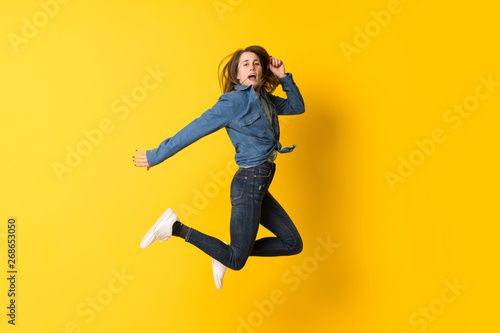 Fototapeta Naklejka Na Ścianę i Meble -  Young woman jumping over yellow background