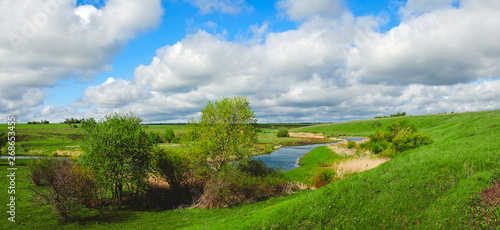 Sunny spring landscape with river and beautiful clouds in blue sky.