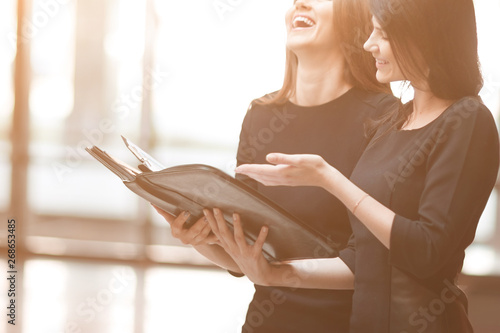two business women read business documents standing in the office lobby.