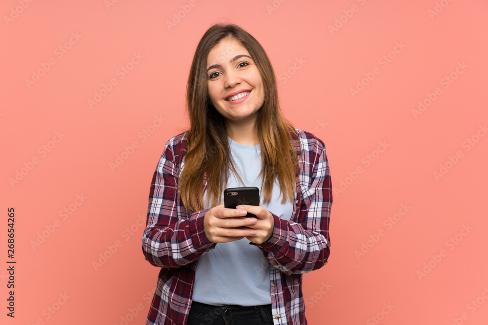 Young girl over pink wall sending a message with the mobile Young girl over pink wall sending a message with the mobile