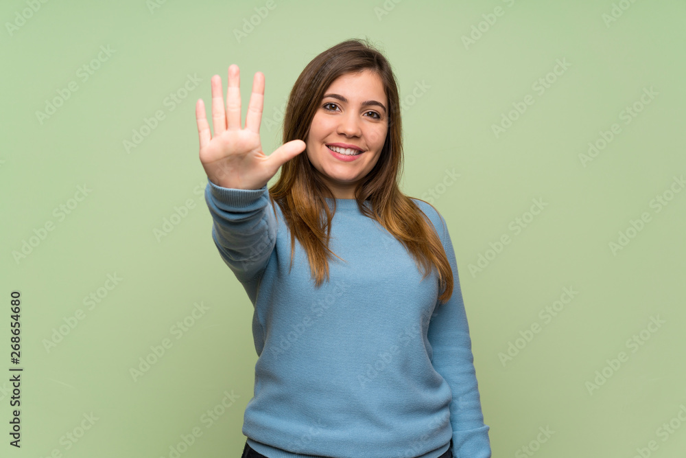 Fototapeta premium Young girl over green wall counting five with fingers