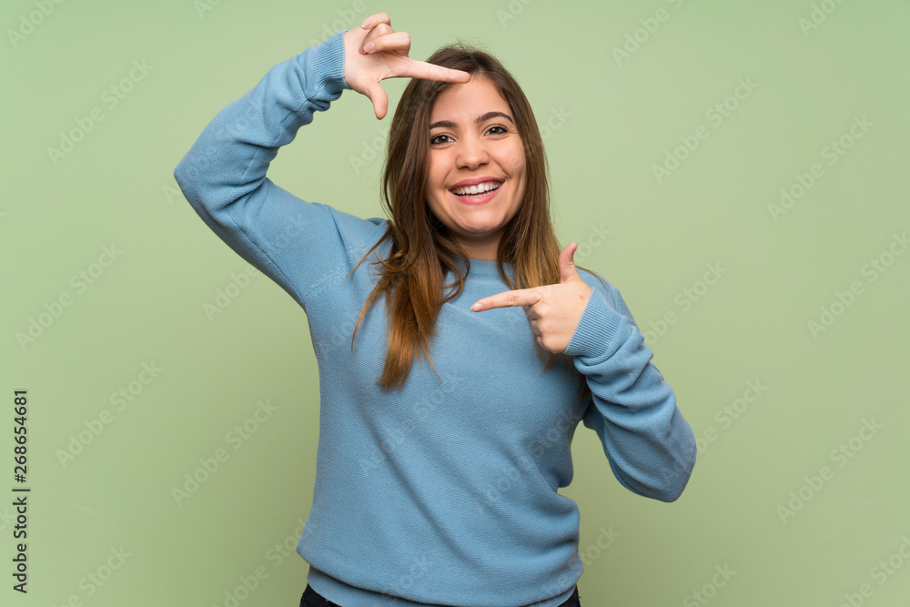 Young girl over green wall focusing face. Framing symbol Young girl over green wall focusing face. Framing symbol