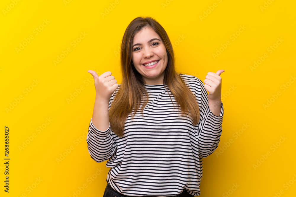 Young girl over yellow wall with thumbs up gesture and smiling Young girl over yellow wall with thumbs up gesture and smiling