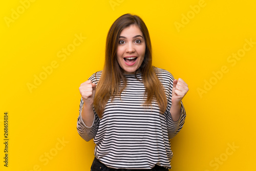 Young girl over yellow wall celebrating a victory in winner position