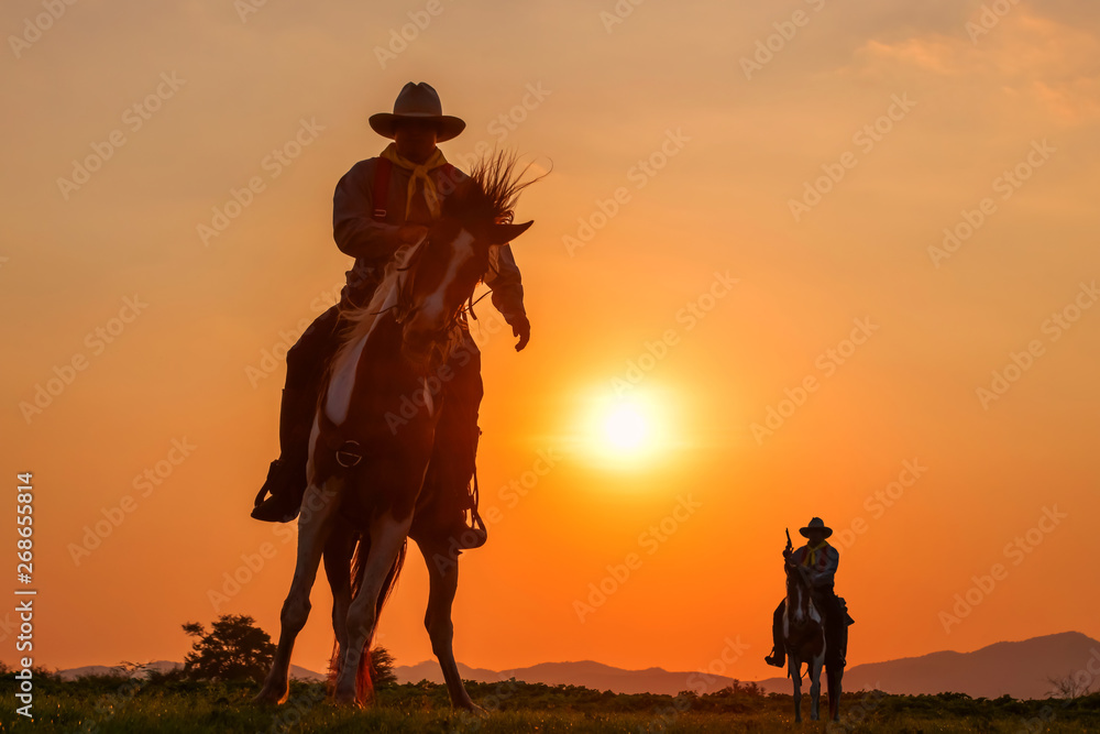 The silhouette of two men wearing a cowboy outfit with a horse and a gun held in the hand