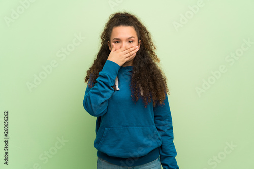 Teenager girl over green wall covering mouth with hands for saying something inappropriate