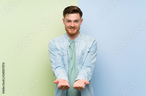 Redhead man over colorful background holding copyspace imaginary on the palm to insert an ad