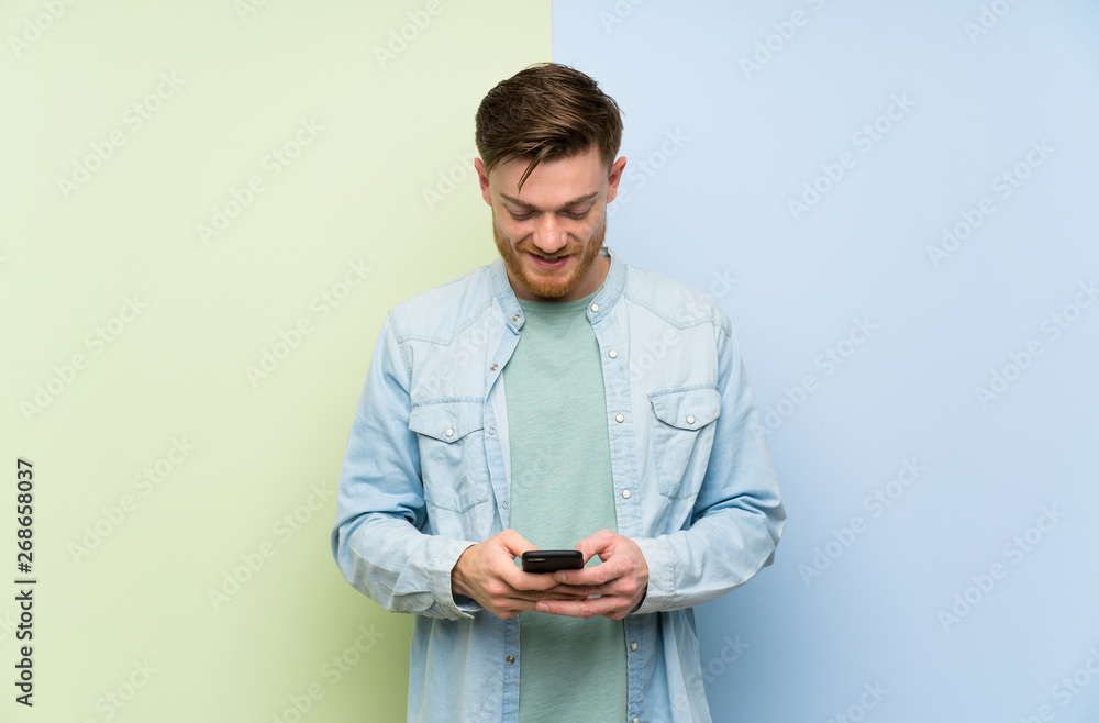 Redhead man over colorful background sending a message with the mobile Redhead man over colorful background sending a message with the mobile