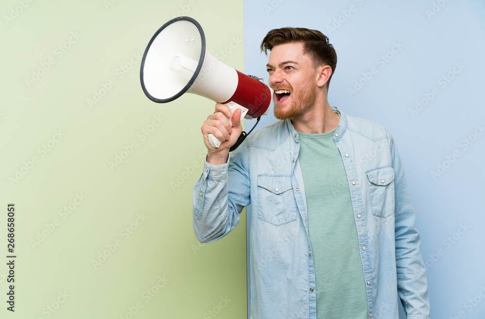 Redhead man over colorful background shouting through a megaphone Redhead man over colorful background shouting through a megaphone