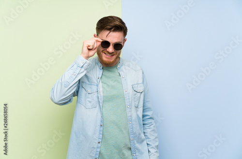 Redhead man over colorful background with glasses and happy