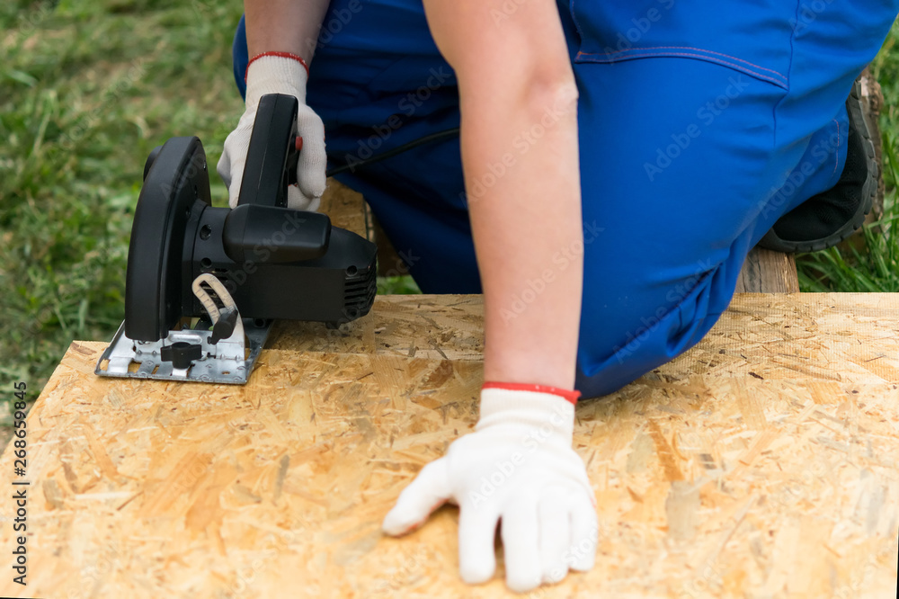 worker's hands hold a circular saw to cut a wooden shield worker's hands hold a circular saw to cut a wooden shield