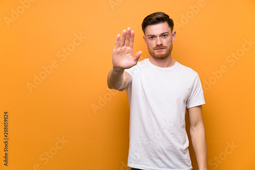 Redhead man over brown wall making stop gesture