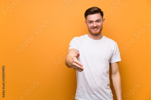 Redhead man over brown wall shaking hands for closing a good deal