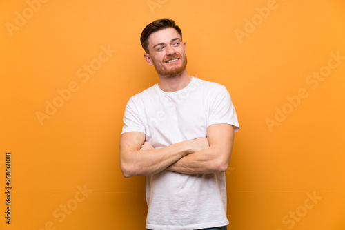 Redhead man over brown wall with arms crossed and happy