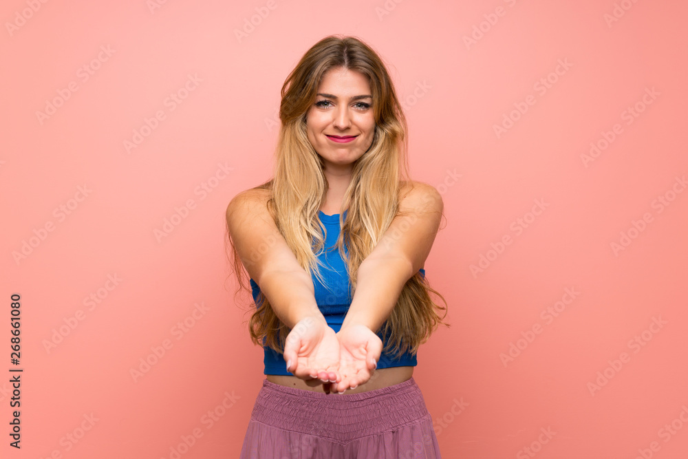Young blonde woman over isolated pink background holding copyspace imaginary on the palm to insert an ad Young blonde woman over isolated pink background holding copyspace imaginary on the palm to insert an ad