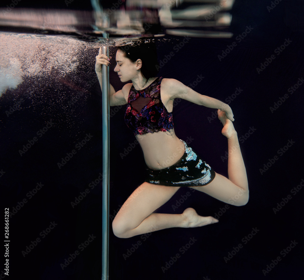 Obraz premium Young, fit, slim woman with pole underwater in the swimming pool on black background
