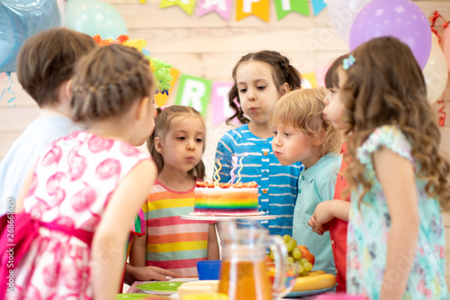 Group of kids celebrating birthday party and blowing candles on cake