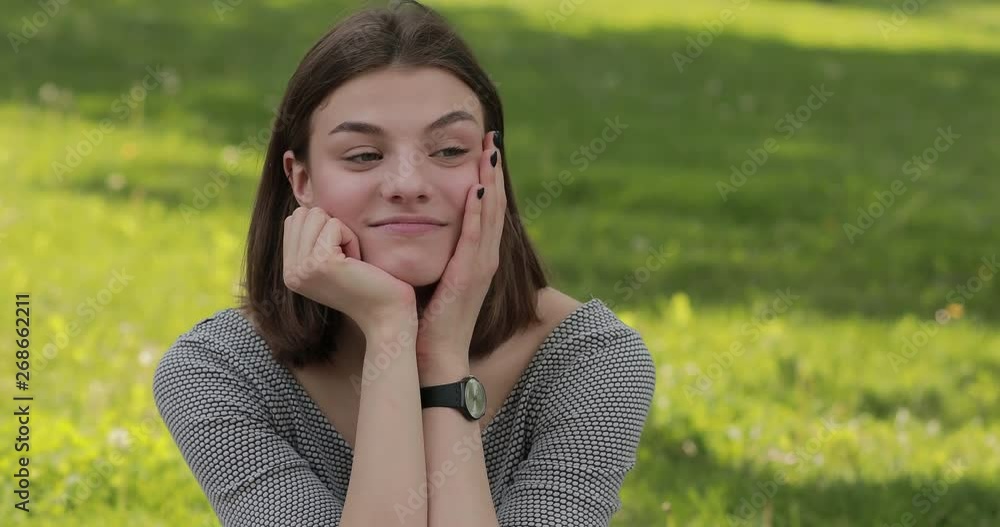 Pretty candid cute woman leaning head on hands sitting in the park tossing hair Pretty candid cute woman leaning head on hands sitting in the park tossing hair