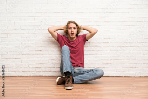 Tableau sur toile Blonde man sitting on the floor frustrated and takes hands on head