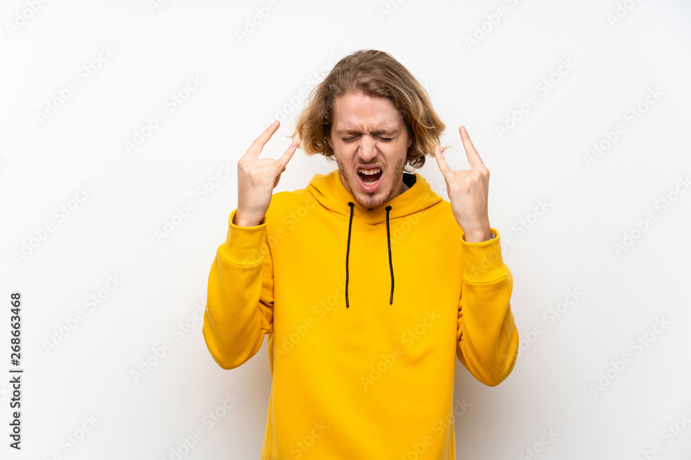 Blonde man with sweatshirt over white wall making rock gesture Blonde man with sweatshirt over white wall making rock gesture