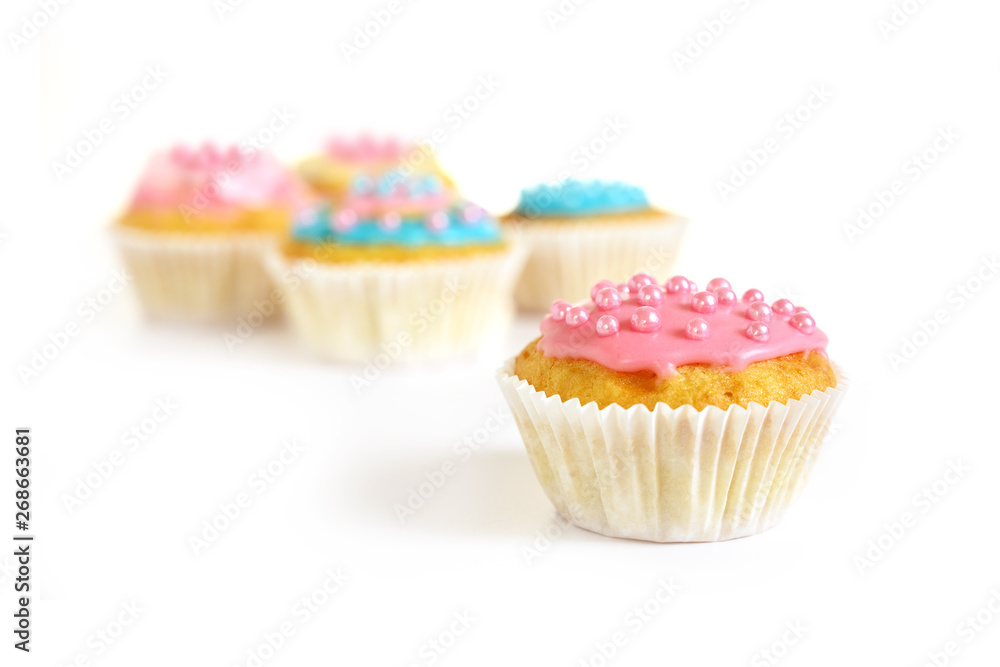 muffin or cupcake with pink icing and sugar pearls, more cupcakes blurry in the background, isolated with shadows on white, copy space muffin or cupcake with pink icing and sugar pearls, more cupcakes blurry in the background, isolated with shadows on white, copy space