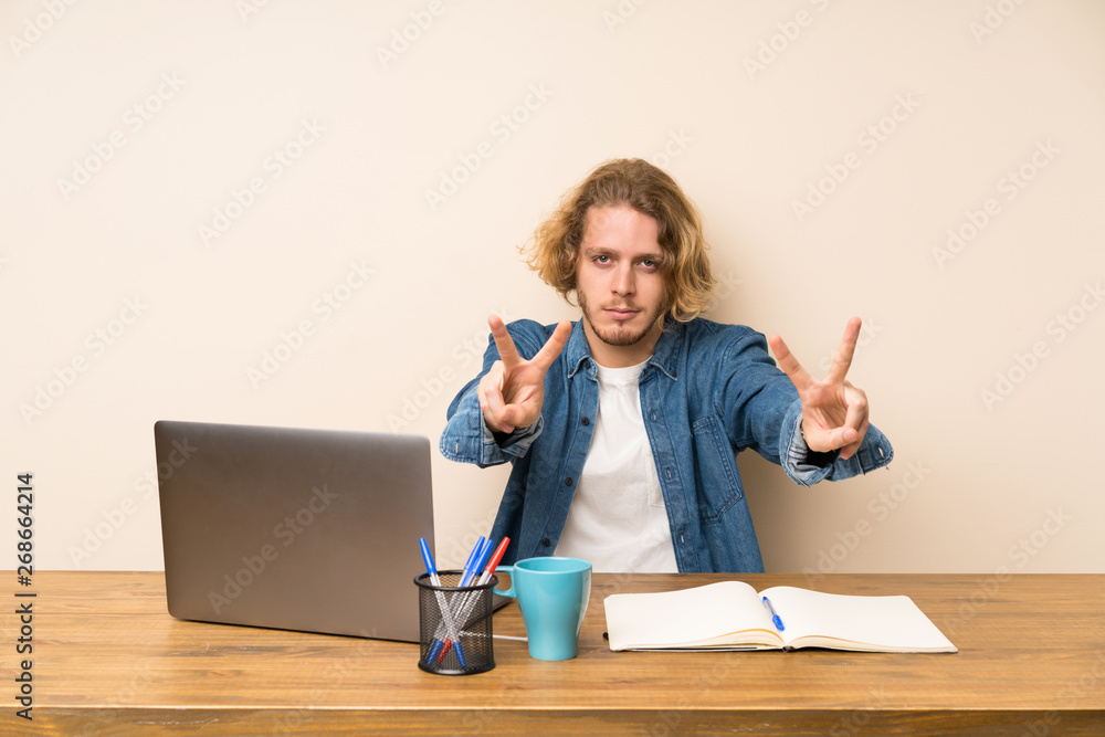 Blonde man with a laptop smiling and showing victory sign Blonde man with a laptop smiling and showing victory sign