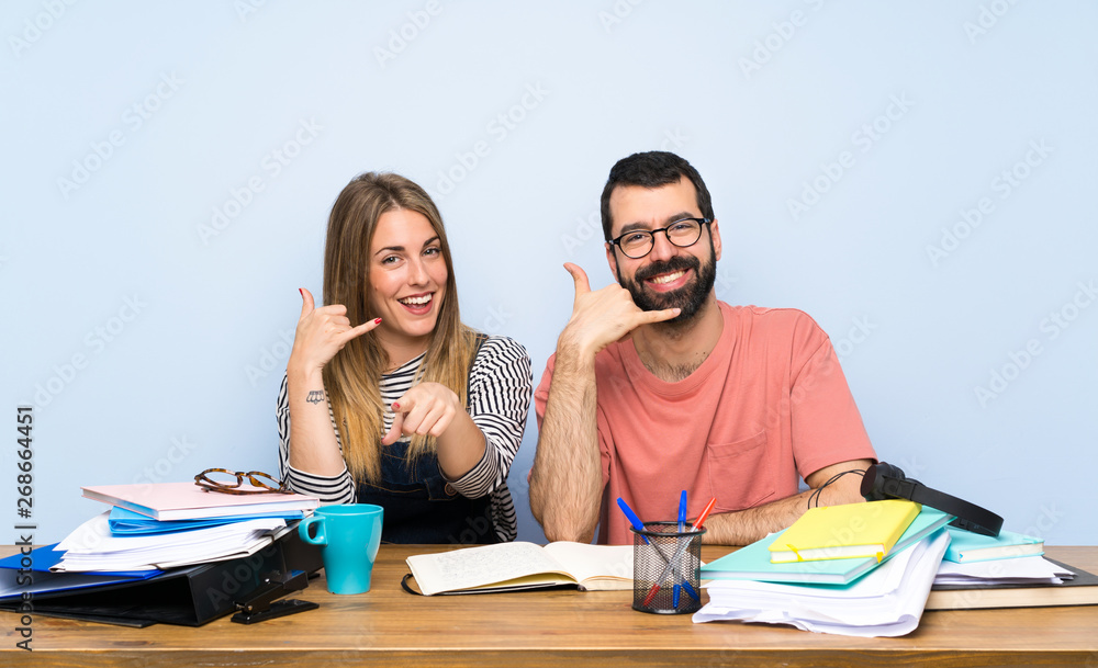 Students with many books making phone gesture and pointing front Students with many books making phone gesture and pointing front