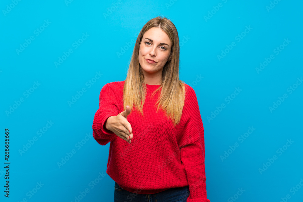 Woman with red sweater over blue wall shaking hands for closing a good deal Woman with red sweater over blue wall shaking hands for closing a good deal