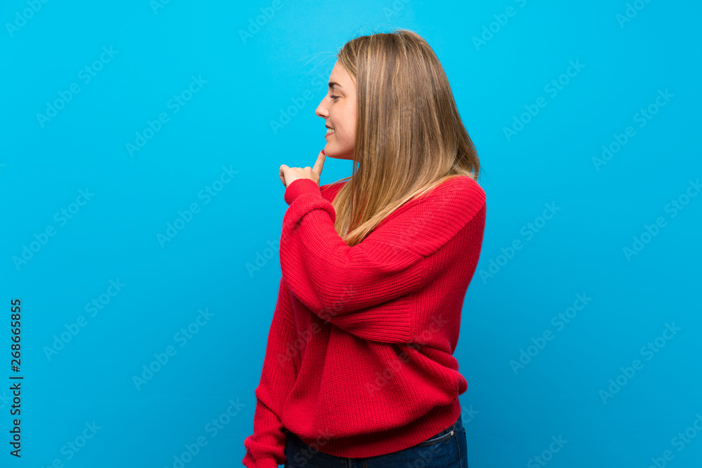 Woman with red sweater over blue wall pointing back Woman with red sweater over blue wall pointing back
