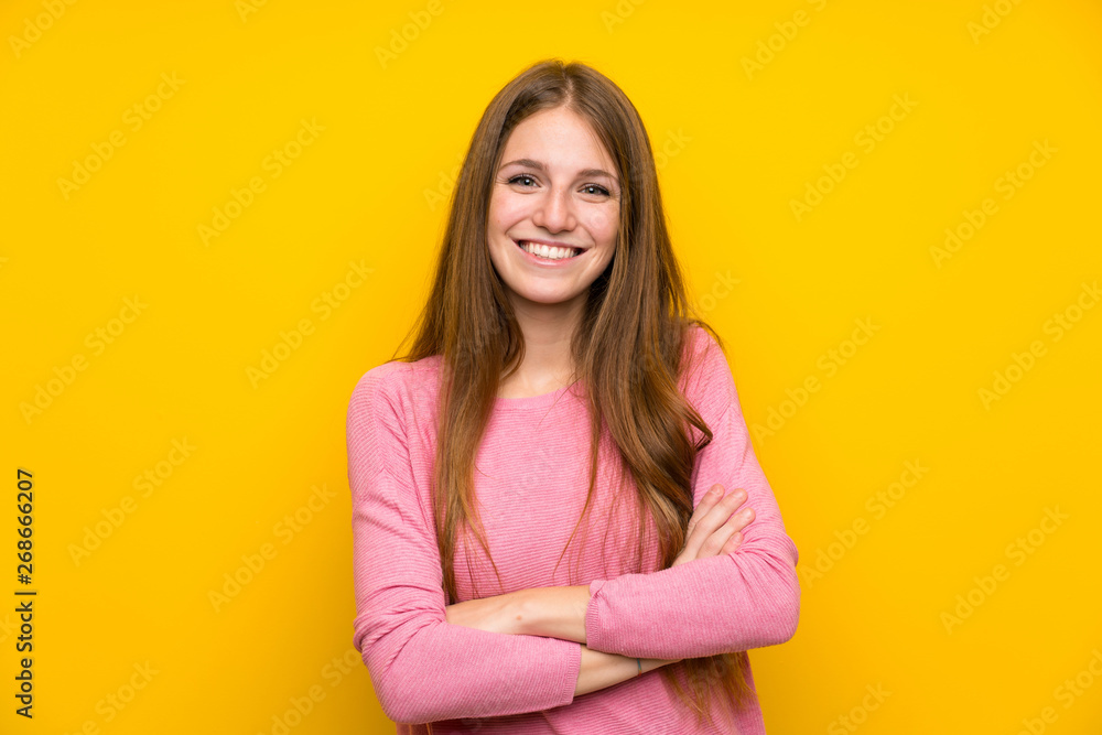 Young woman with long hair over isolated yellow wall keeping the arms crossed in frontal position Young woman with long hair over isolated yellow wall keeping the arms crossed in frontal position