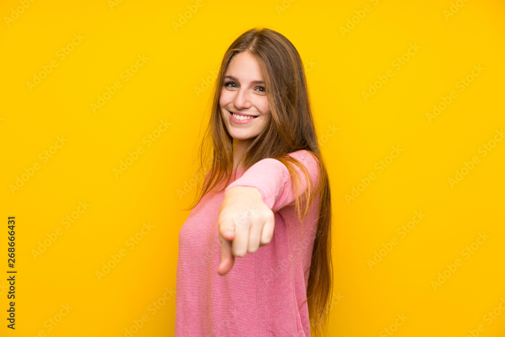Obraz premium Young woman with long hair over isolated yellow wall points finger at you with a confident expression