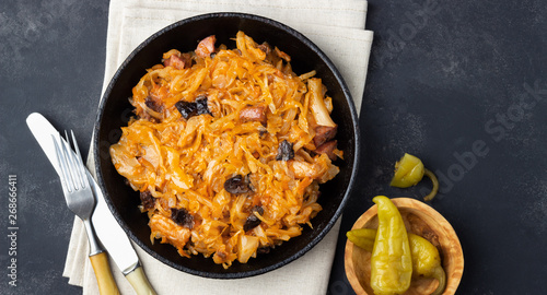 Traditional dish of polish cuisine - Bigos from fresh cabbage, meat and prunes. Top view. Dark background.