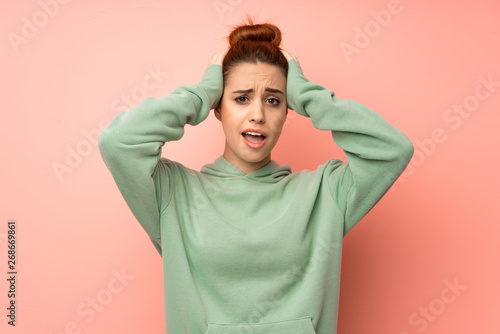 Young redhead woman with sweatshirt frustrated and takes hands on head © luismolinero