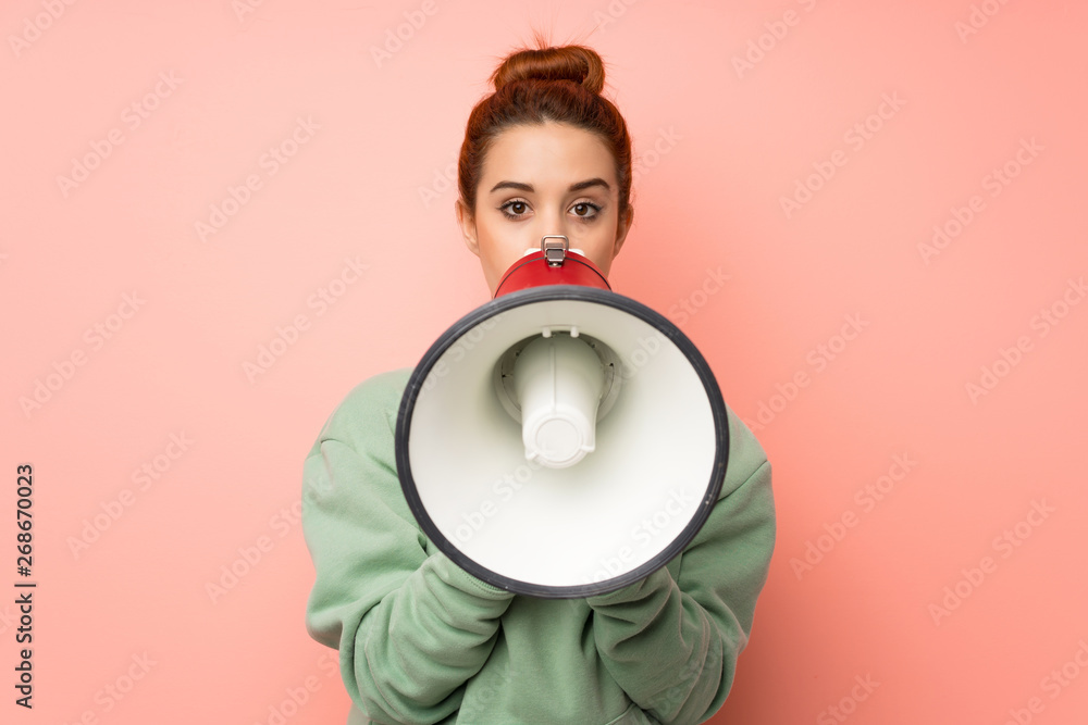 Young redhead woman with sweatshirt shouting through a megaphone Young redhead woman with sweatshirt shouting through a megaphone
