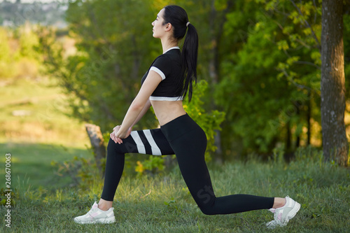 Sexy, sporty girl with a beautiful figure wearing a sports brassiere and leggings, doing sport exercises, outdoor stretching