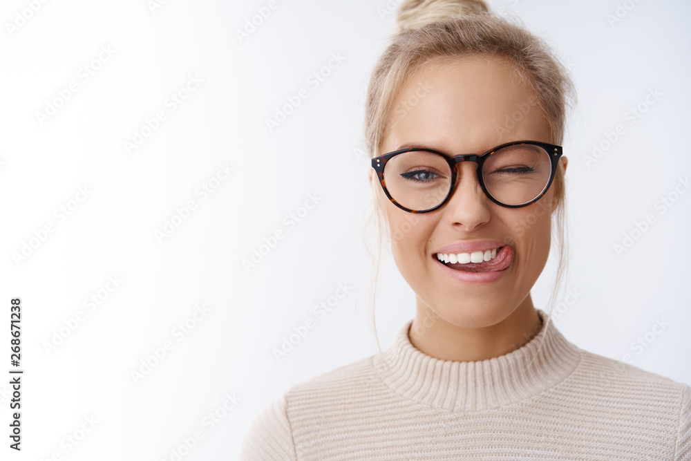 Close-up shot of flirty and playful caucasian blond woman in glasses combed haircut winking happily with positive attitude showing tongue enjoying weekends over white background Close-up shot of flirty and playful caucasian blond woman in glasses combed haircut winking happily with positive attitude showing tongue enjoying weekends over white background