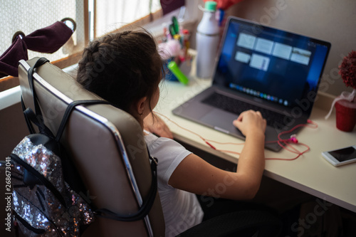 Little girl sitting in chair and using laptop after school