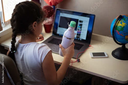 Little girl looking in laptop with thermo bottle for water in hand