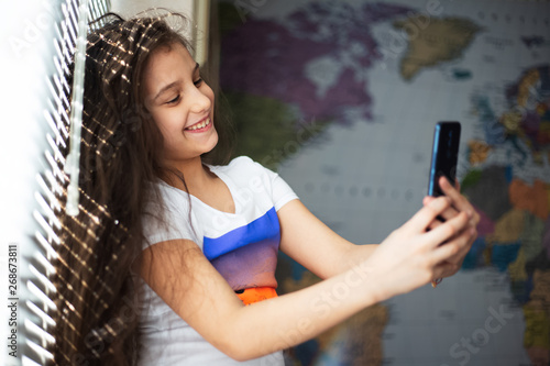 Portrait of cheerful modern children girl with smartphone in hands  on background of world map