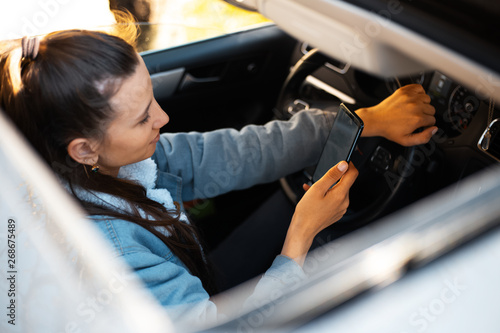 Young girl driving the car with smartphone in hand