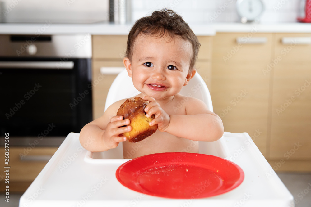 Smiling baby in high chair holding muffin Smiling baby in high chair holding muffin