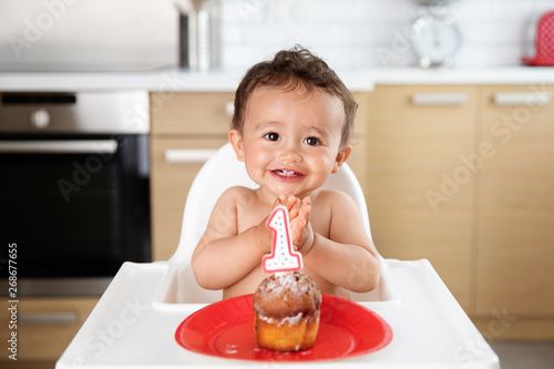 Happy baby in high chair with cake celebrating first birthday