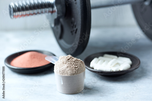 Scoop of Whey Protein, Beta-alanine capsules, Creatine Powder and a dumbbell in background. Sport nutrition. Stone / Wooden background. Copy space photo
