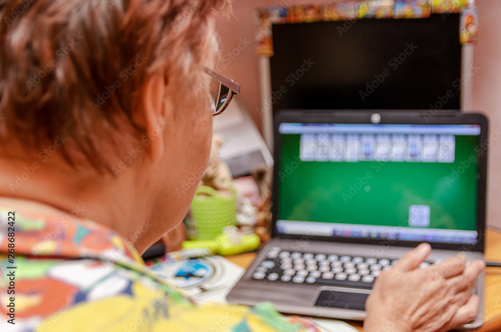 Old woman with glasses plays a computer game on a laptop. Photo from the back Old woman with glasses plays a computer game on a laptop. Photo from the back