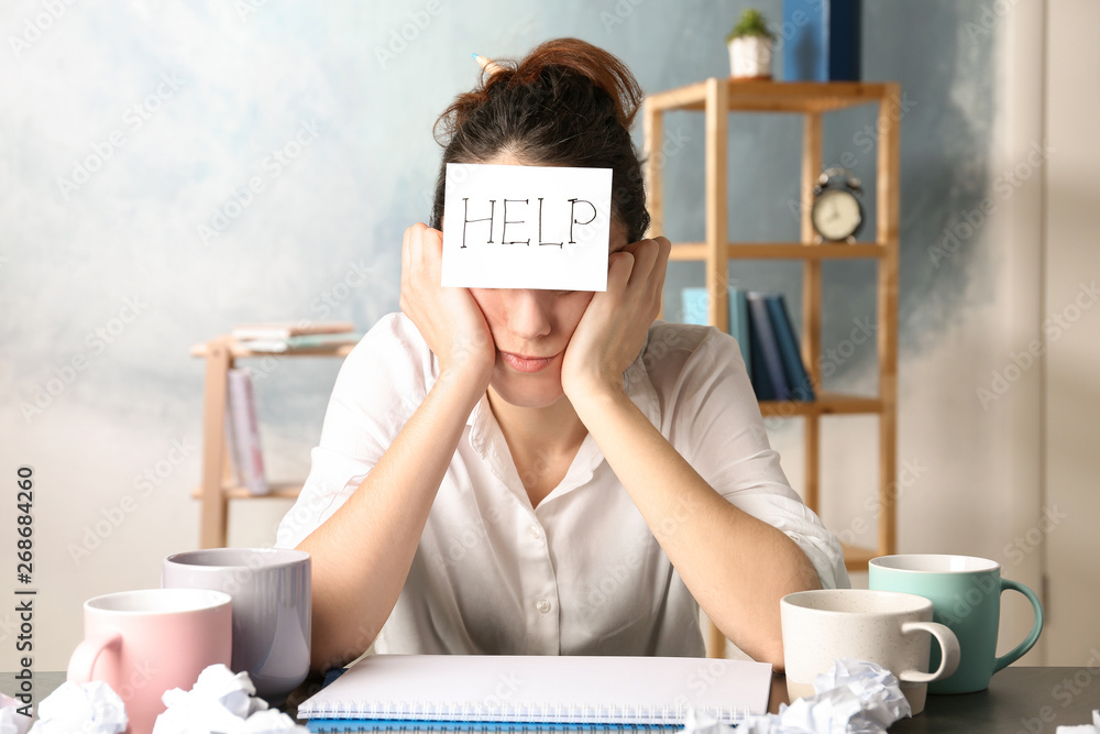 Fotografie Young woman with note HELP on forehead at workplace