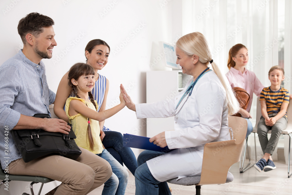 Cute child sitting with her parents and giving high five to doctor in hospital